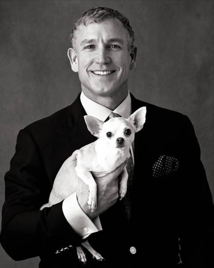 Black and white portrait of Dr. Robert Tomlinson in a suit, holding his chihuahua